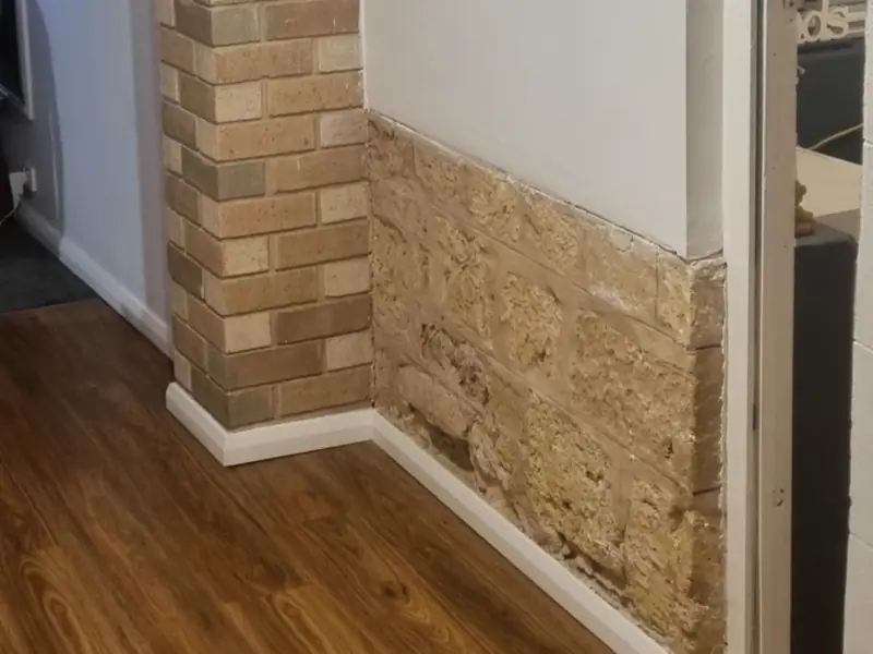 A brick pillar beside an exposed sandstone lower wall and a new timber-look floor