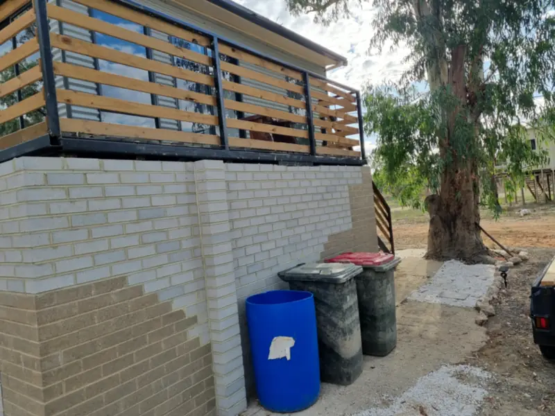 Corner of a timber-slat deck over a painted brick base, with wheelie bins below