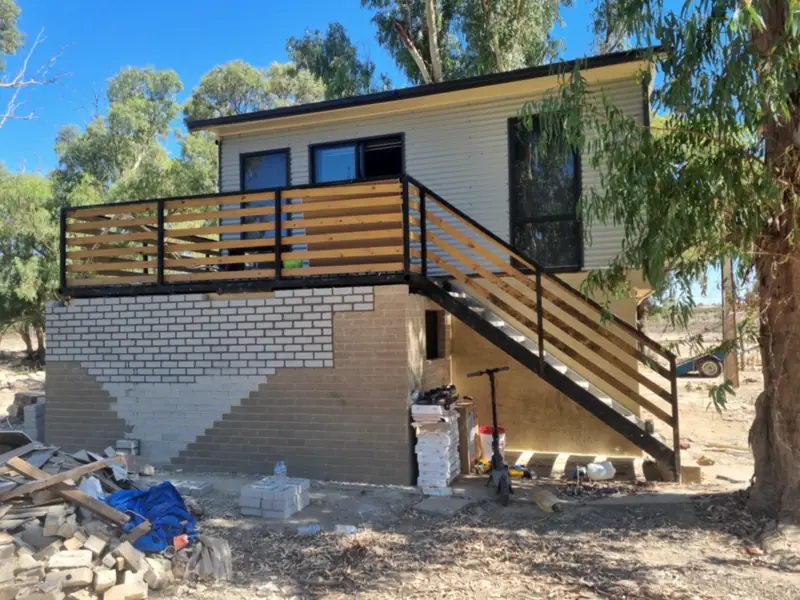 A raised house part-way through a job, with the brick base half painted and building materials in the yard