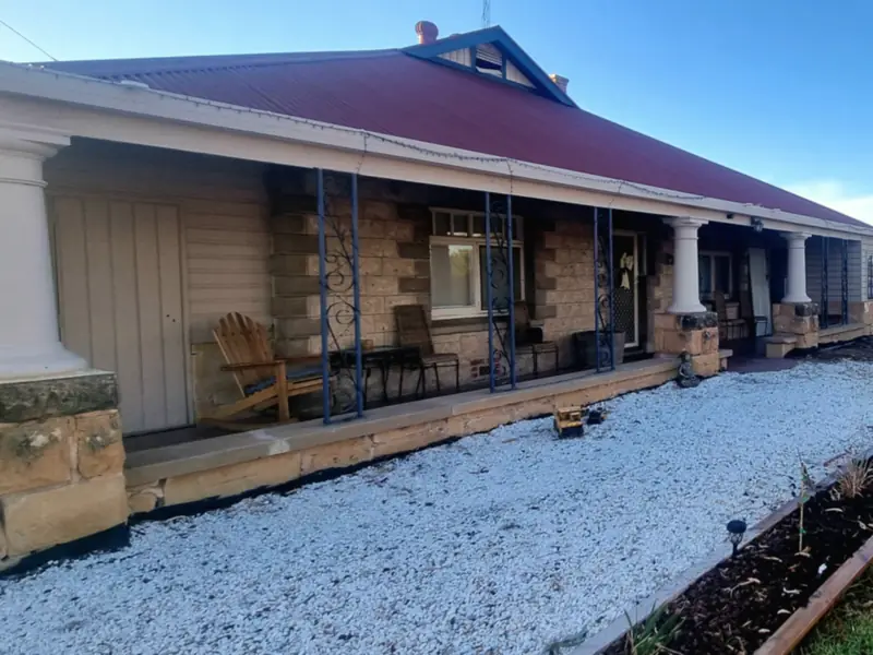A stone homestead verandah with a new white gravel path and an edged garden bed