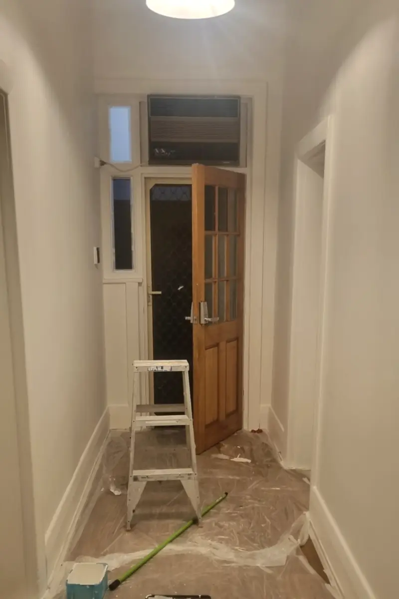 Hallway before: drop sheets on the floor, a ladder and a paint roller out