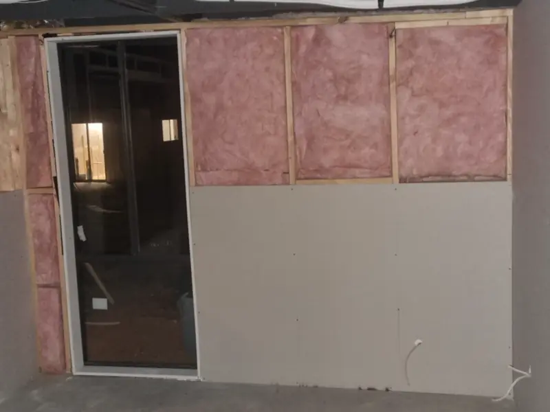 A wall with pink insulation batts in the frame and the lower half sheeted