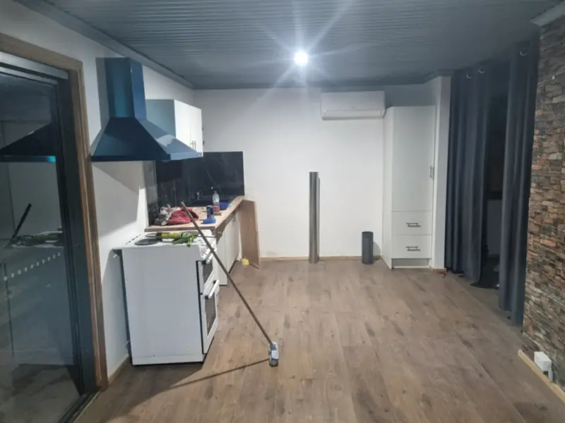 A kitchen space with a dark ceiling, white cupboards and a new timber-look floor