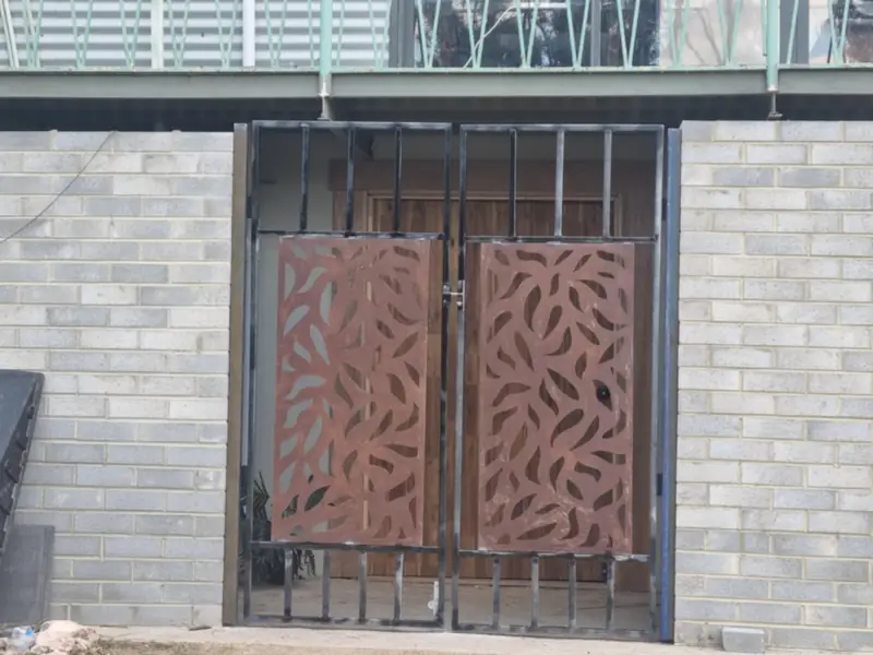 Rust-red laser-cut screen gates set in a steel frame between brick walls, under a balcony
