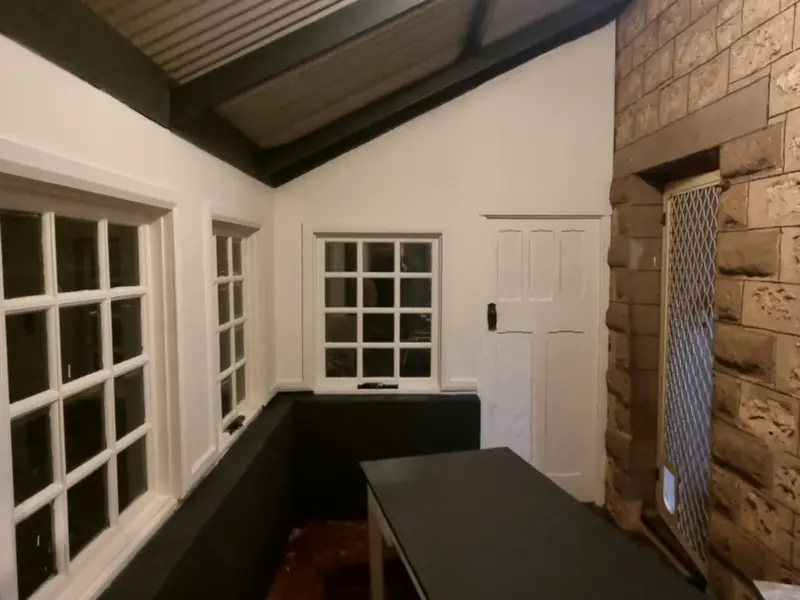 A sunroom with white timber windows and a sandstone feature wall